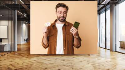 Serious man holding credit card using mobile phone. Wall mural