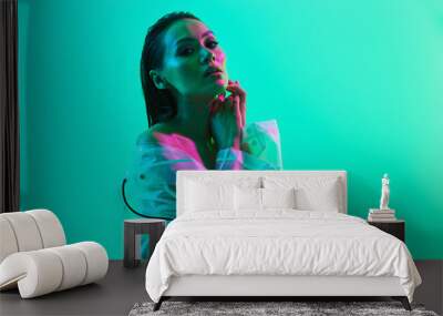 Serious woman posing isolated over blue wall background with neon bright lights dressed in raincoat. Wall mural