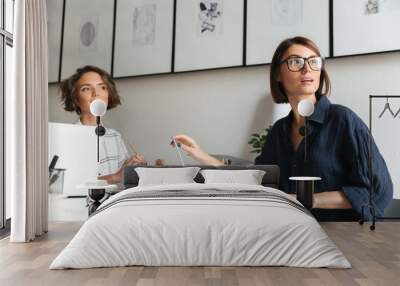 Side view of two pretty women sitting by the table Wall mural