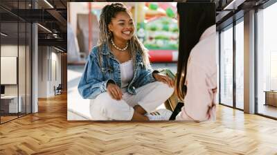 Smiling african american woman talking with her friend while sitting in amusement park Wall mural