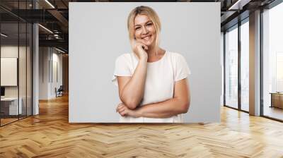 Smiling beautiful young amazing blonde woman posing isolated over grey wall background dressed in basic white t-shirt. Wall mural