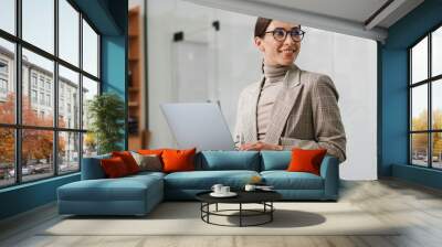 Smiling charming woman in eyeglasses working with laptop at office Wall mural