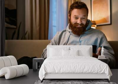 Smiling father using smartphone while resting with his son on couch Wall mural