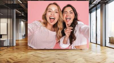 Smiling friends women posing isolated over pink wall background take selfie by camera. Wall mural