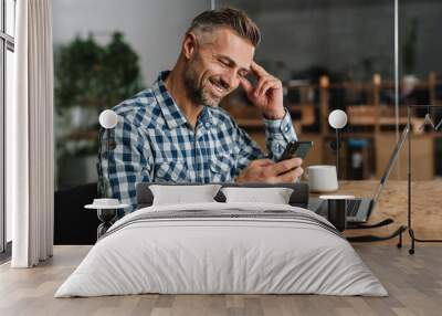 Smiling grey man using mobile phone while working with laptop Wall mural