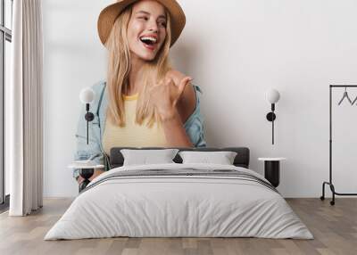 Smiling happy amazing young pretty woman wearing hat posing isolated over white wall background pointing to copyspace. Wall mural