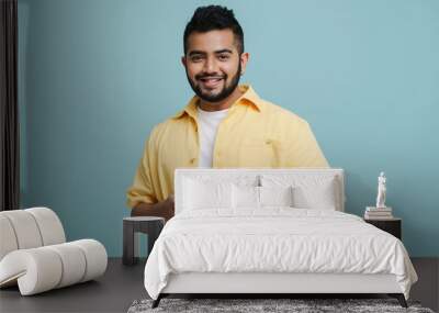 Smiling indian guy using mobile phone isolated over blue wall Wall mural