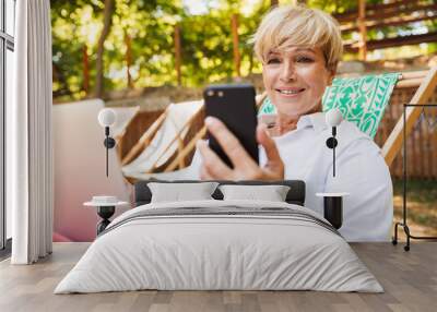 Smiling mature woman holding mobile phone Wall mural