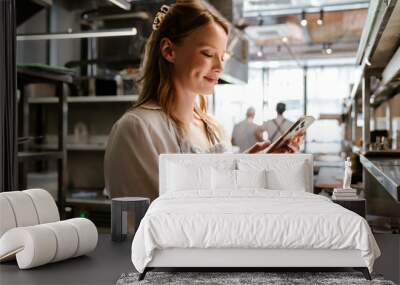 Smiling woman cook using mobile phone while standing in kitchen of a restaurant Wall mural