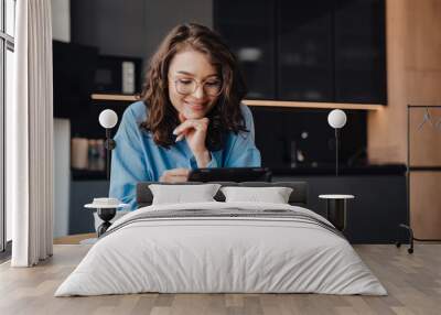 Smiling woman drinking coffee and using tablet computer while sitting in kitchen Wall mural