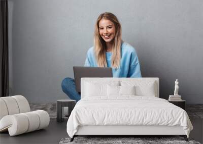 Smiling young blonde girl using laptop computer Wall mural