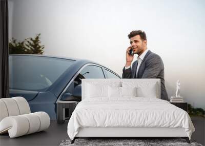 Smiling young businessman in suit standing at his car Wall mural