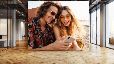 Smiling young loving couple using mobile phone Wall mural