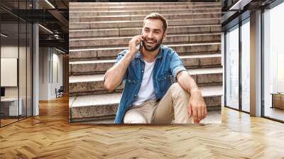 Smiling young man sitting on stairs outdoors Wall mural