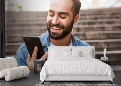 Smiling young man using mobile phone Wall mural