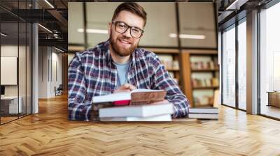 Smiling young student sitting at the desk in library Wall mural