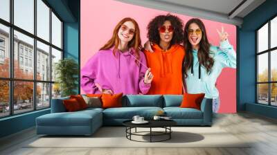 Three happy young girls wearing colorful hoodies standing Wall mural