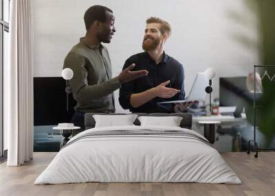 Two cheerful businessmen dicussing something on the laptop and smiling Wall mural