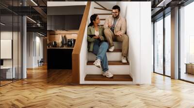 Two cheerful coworkers talking while sitting on stairs in office kitchen Wall mural