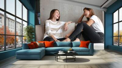 Two cheerful girls talking while sitting at home Wall mural