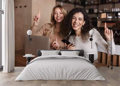 Two cheerful young girls friends sitting at the cafe table Wall mural