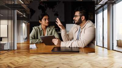 Two coworkers discussing business details and working on tablet while sitting in office Wall mural