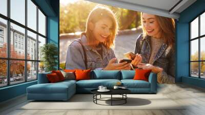 Two happy exited young woman friends looking at smartphones in park outdoor Wall mural