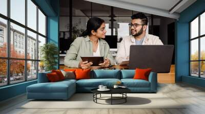 Two indian colleagues using laptop and tablet while working together in office Wall mural