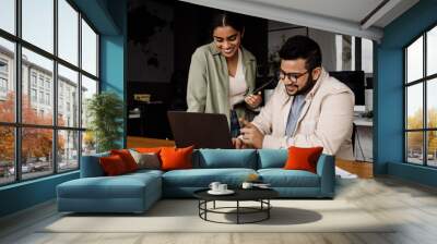 Two indian colleagues using laptop and tablet while working together in office Wall mural