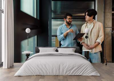 Two male colleagues discussing project while working in office Wall mural