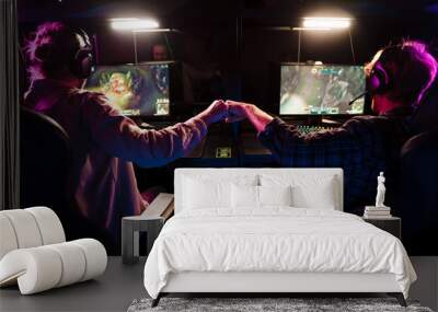 Two male gamers giving fist bump while playing video game together in cybersport club Wall mural