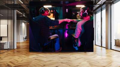 Two male gamers giving fist bump while playing video game together in cybersport club Wall mural