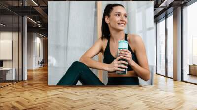 White brunette woman smiling and drinking water while working out Wall mural