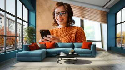 White woman smiling and using mobile phone while working in office Wall mural