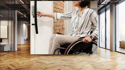 White young woman in wheelchair opening door at office Wall mural