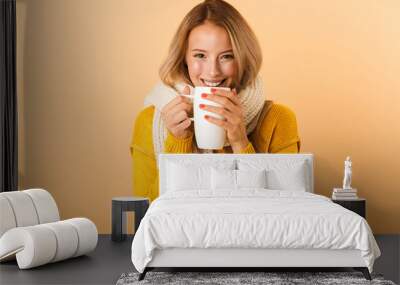 Woman holding cup of tea wearing scarf posing isolated over yellow wall background. Wall mural