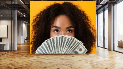 Woman posing isolated over yellow background holding money covering face. Wall mural