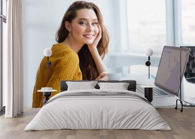 Woman sitting at the table with laptop and drinking tea Wall mural