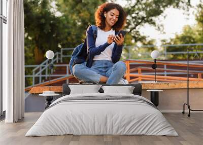 Woman sitting outdoors in park using mobile phone listening music with earphones. Wall mural