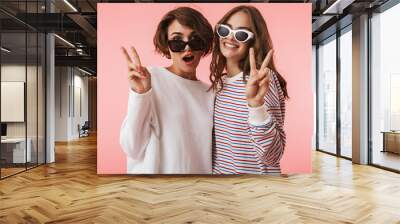 Women friends isolated over pink wall background showing peace gesture. Wall mural