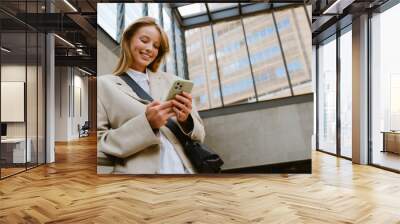 Young beautiful smiling happy woman holding and using her phone Wall mural