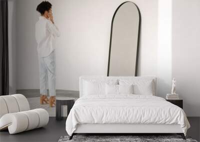 Young black woman standing and looking at mirror indoors Wall mural