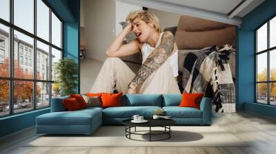 Young blonde woman listening music with earphones and singing while sitting on floor Wall mural