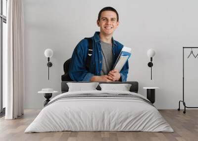 Young brunette student man smiling while holding exercise books Wall mural