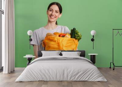 Young brunette woman smiling while holding textile bag with vegetable Wall mural