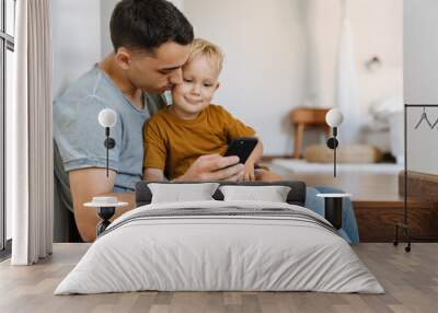 Young father and son using mobile phone while sitting on stairs Wall mural