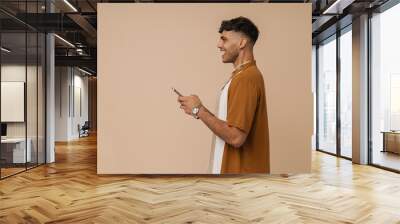 Young handsome stylish smiling man in necklace holding his phone Wall mural