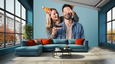 Young happy girl with birthday cake covering eyes of excited guy Wall mural