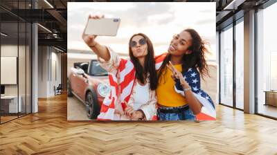 Young happy smiling cheery women friends posing near car outdoors at the beach. Wall mural