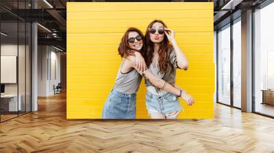 Young happy women friends standing over yellow wall Wall mural